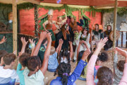 Children raising hands during an imaginative play performance with costumed characters at Hobbledown Heath, West London