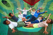 Children laughing and lying on a giant outdoor net climbing structure at Hobbledown Heath adventure village, Hounslow