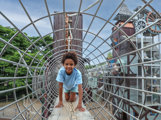 Child crawling through a circular rope tunnel climbing frame at Hobbledown Heath adventure park, Hounslow, West London